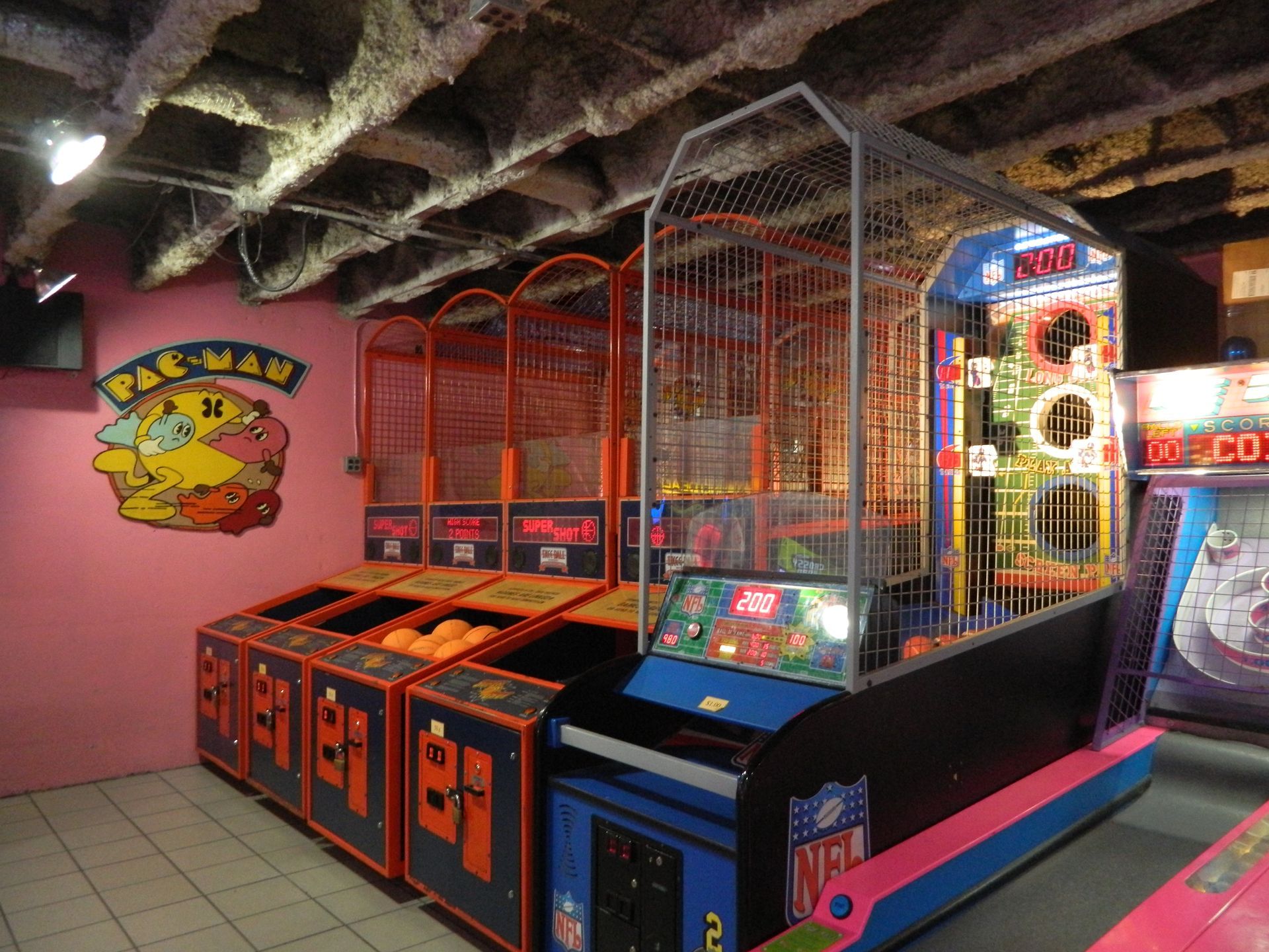 Arcade game room with basketball toss games and Pac-Man wall art.