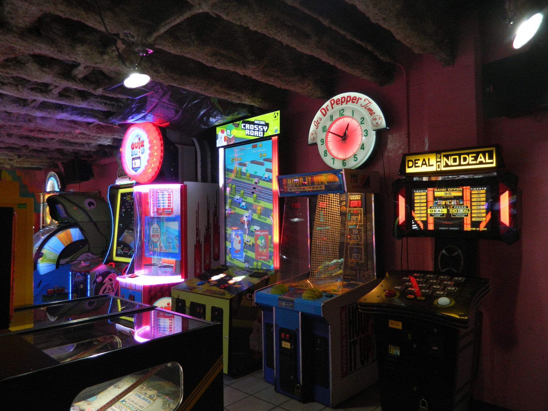 Arcade with various illuminated game machines under a low, dark ceiling; neon signs.