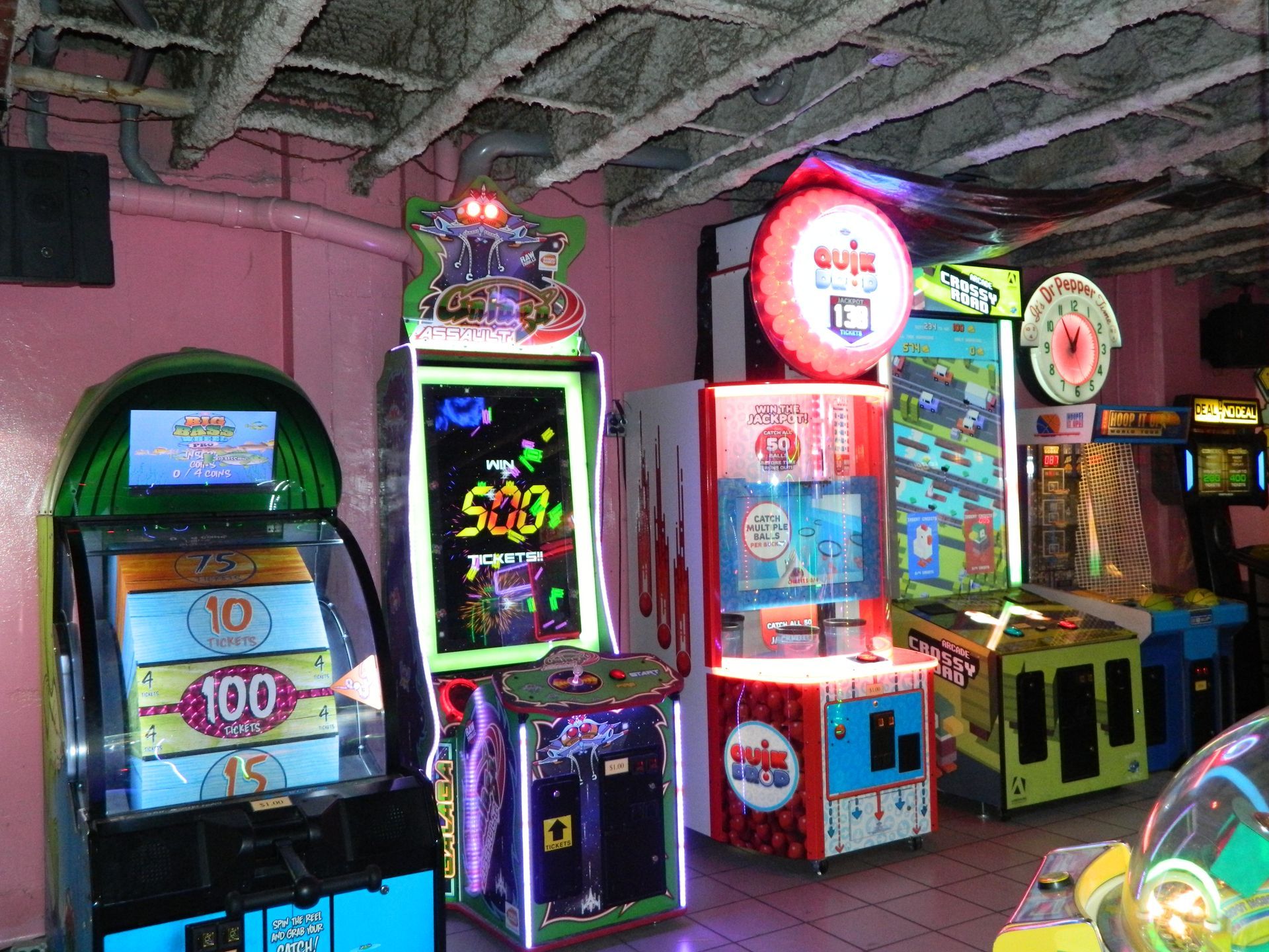 Arcade with brightly lit prize games in a room with pink walls and a textured ceiling.