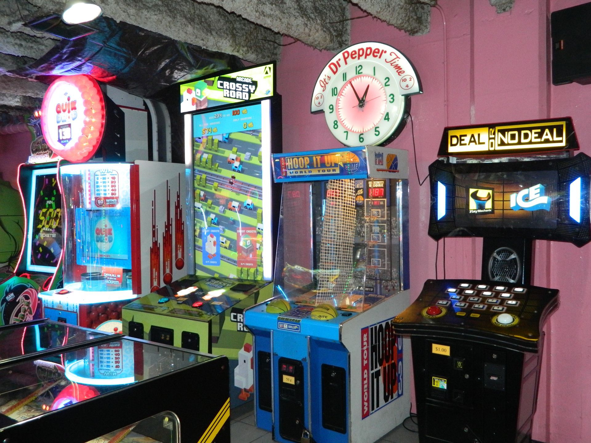 Arcade with various brightly lit game machines against a pink wall, including a Dr. Pepper clock.