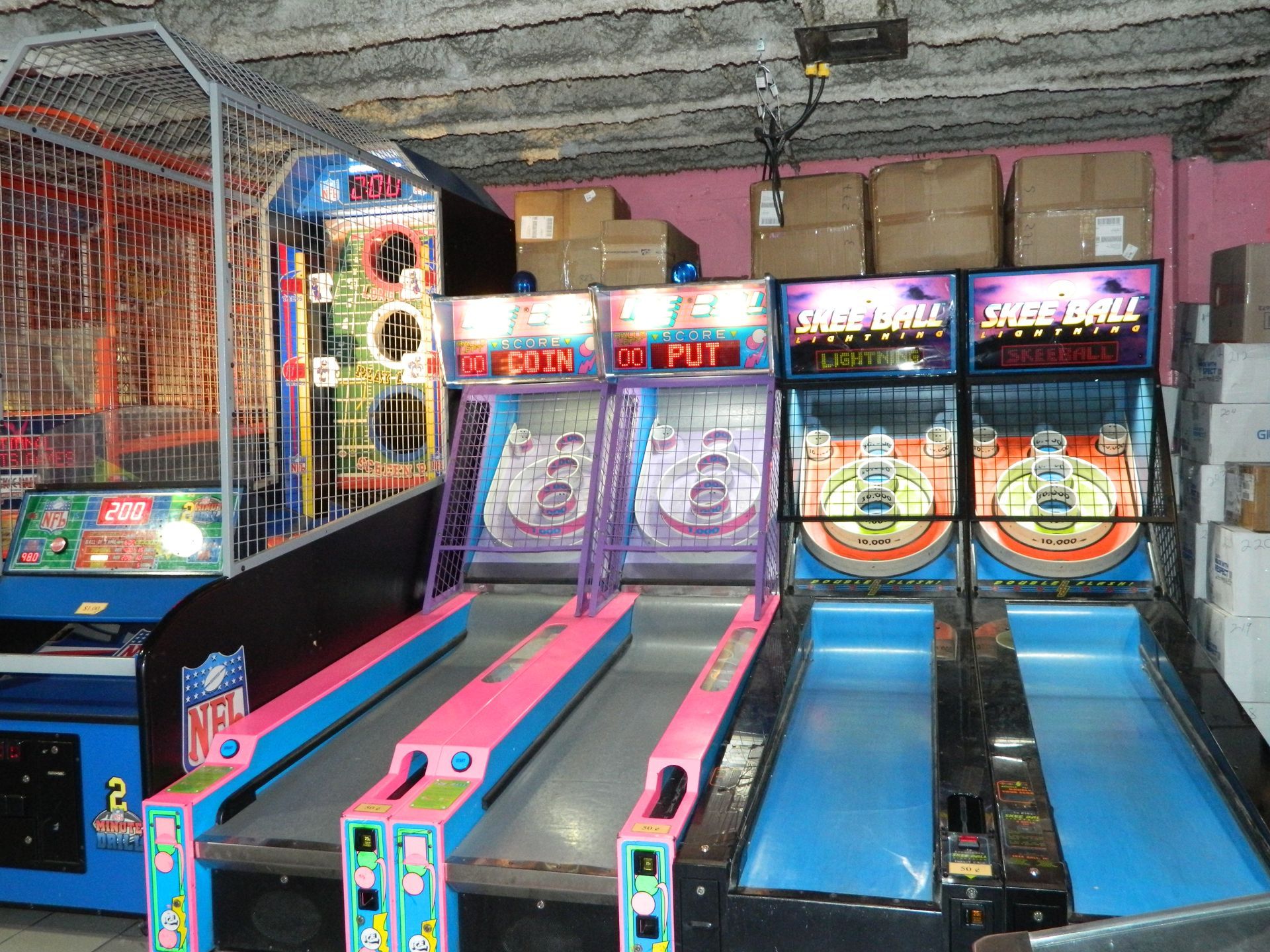 Arcade games: Skee-Ball machines with a ball return lane, two arcade games, and boxes in the background.