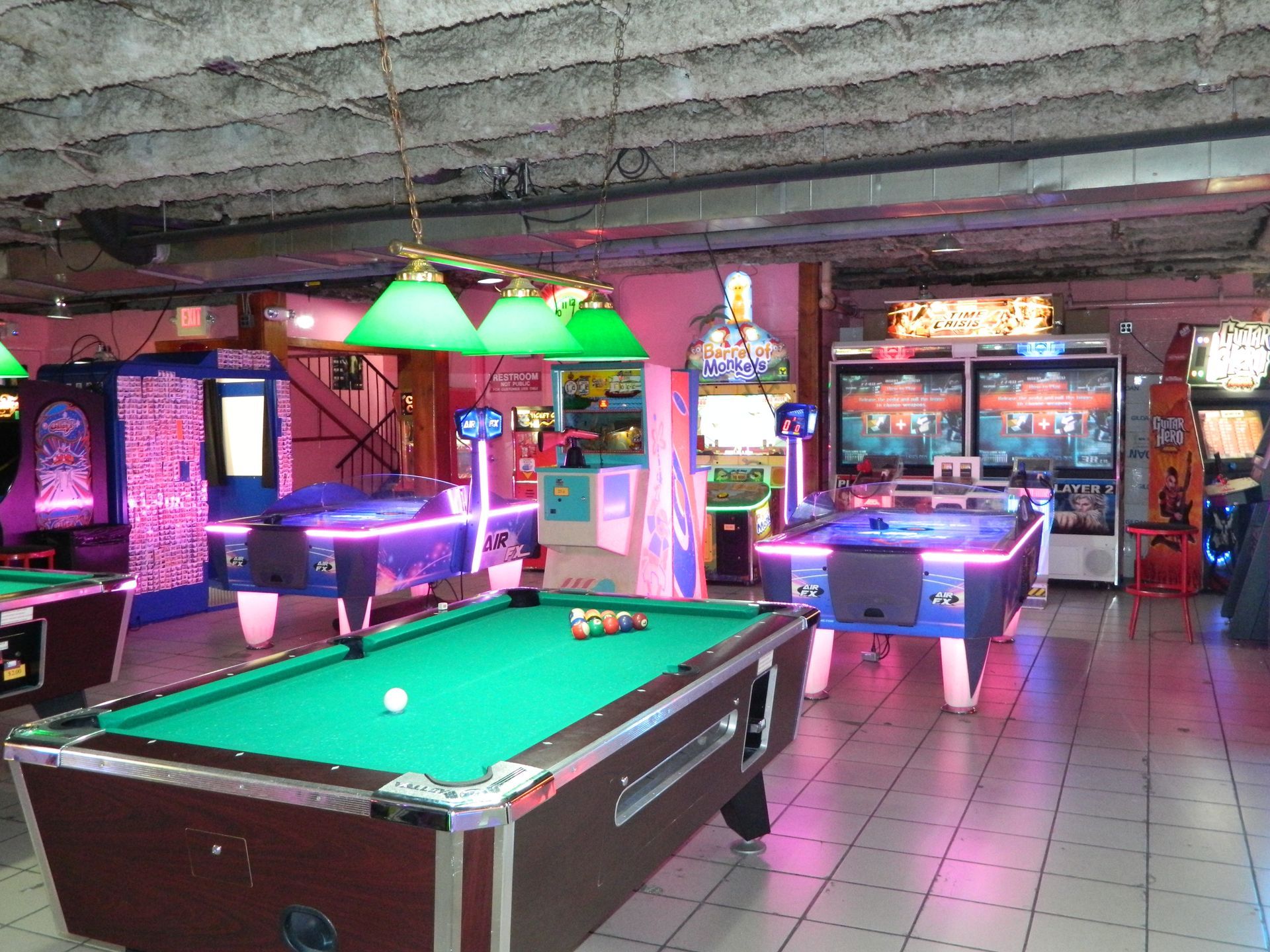 An arcade with a pool table, air hockey, and various game machines, brightly lit.