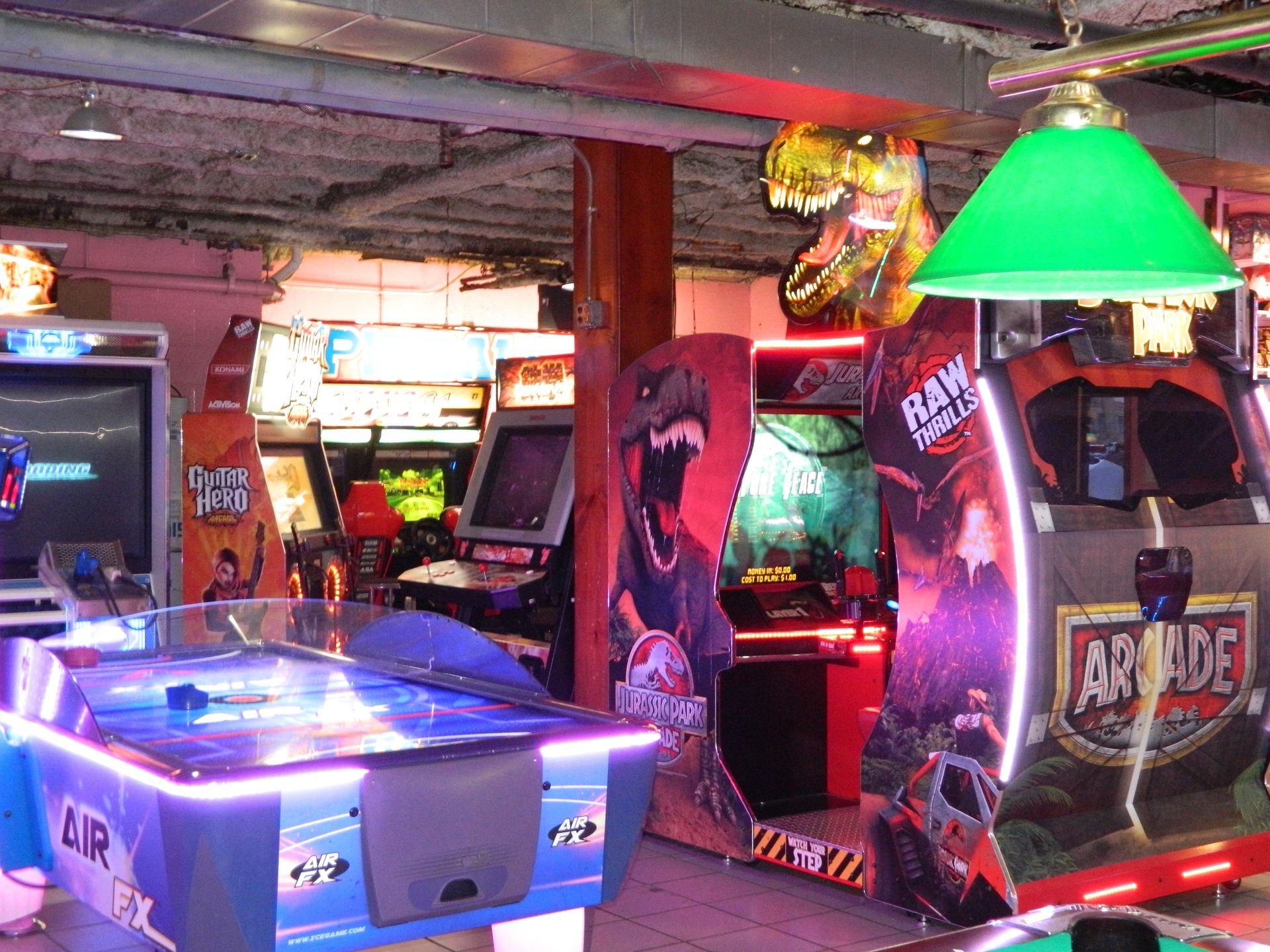Arcade with brightly lit games, including an air hockey table and dinosaur-themed machines.