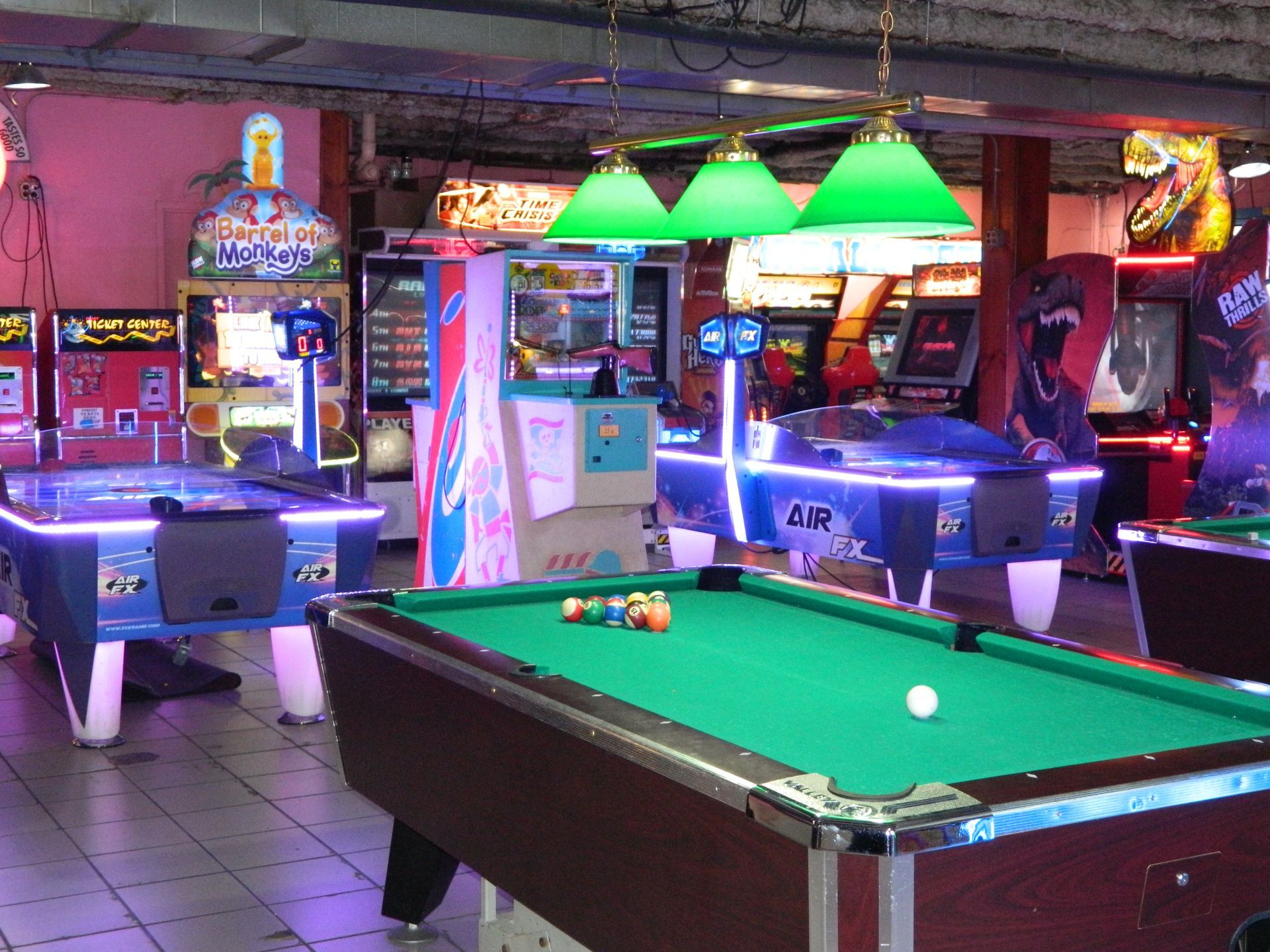 Game room with pool table, air hockey, and arcade games; neon lights.