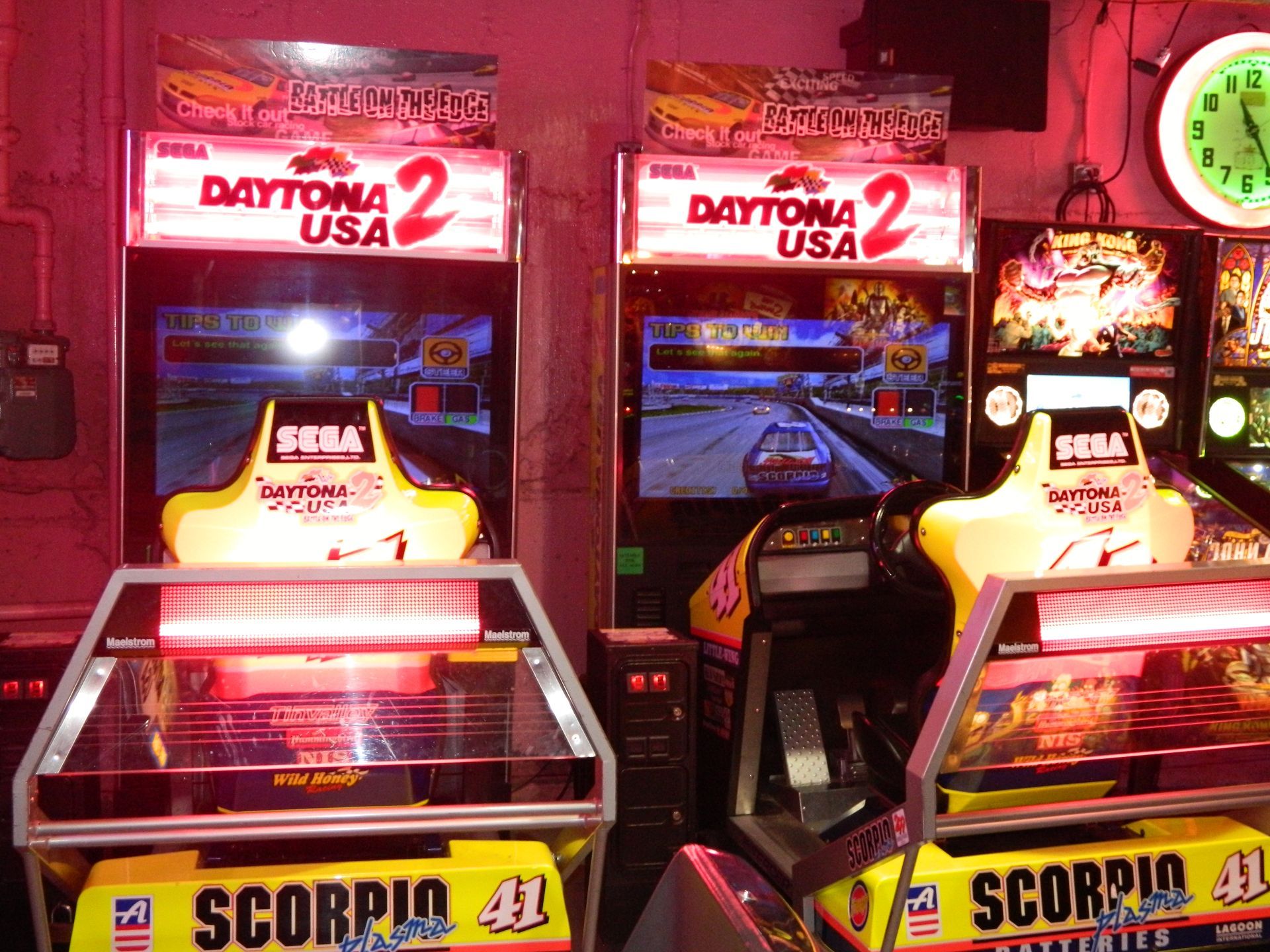 Two Daytona USA 2 arcade machines side by side, brightly lit, showing a racing game on screen.