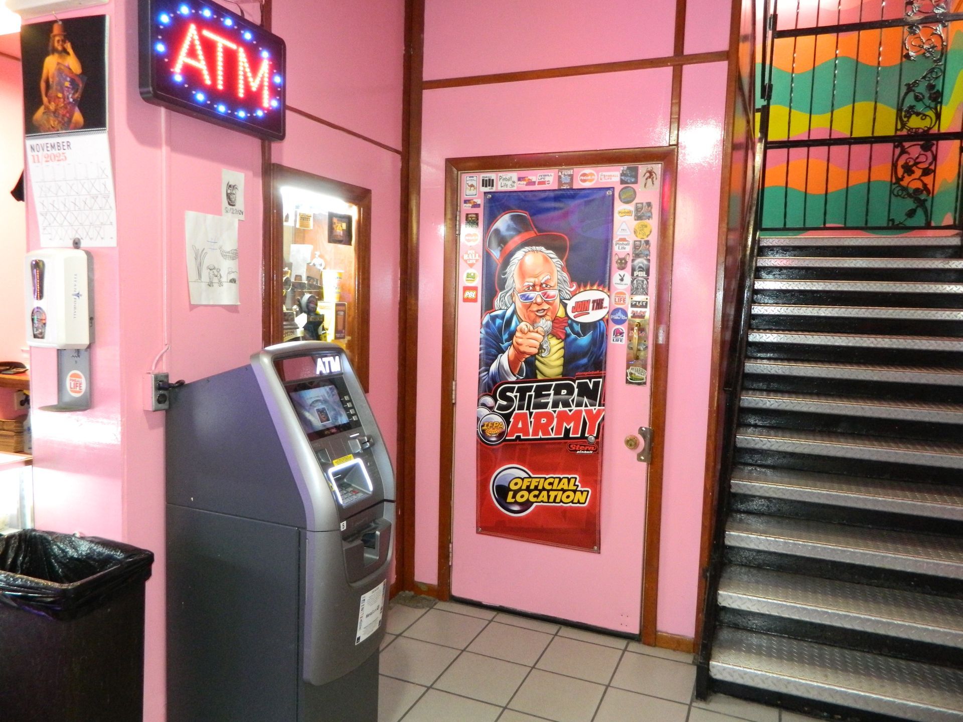 An ATM next to a black trash can inside a pink-painted doorway. 