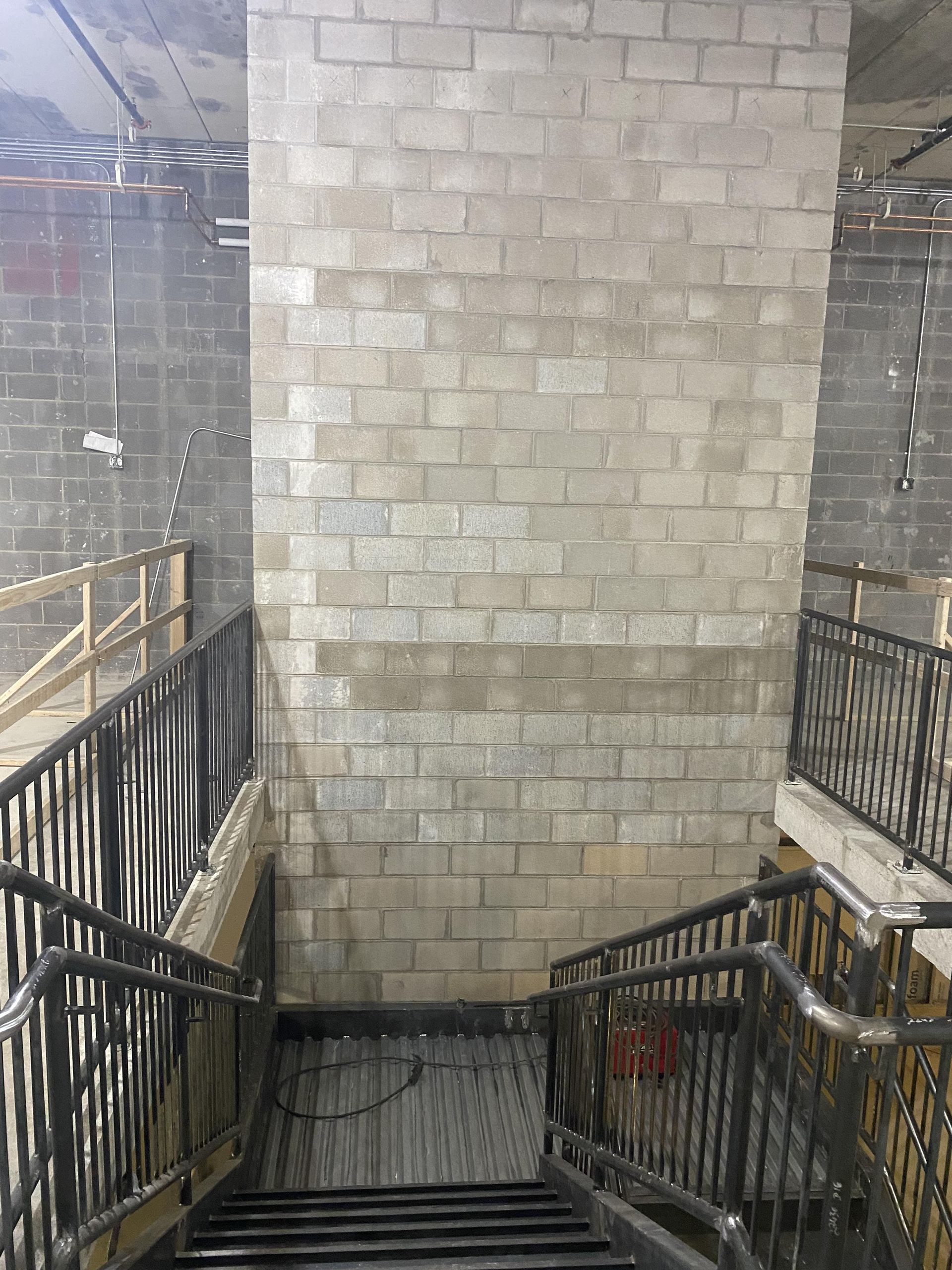 Staircase leading down with metal handrails and a concrete block wall in a construction setting.