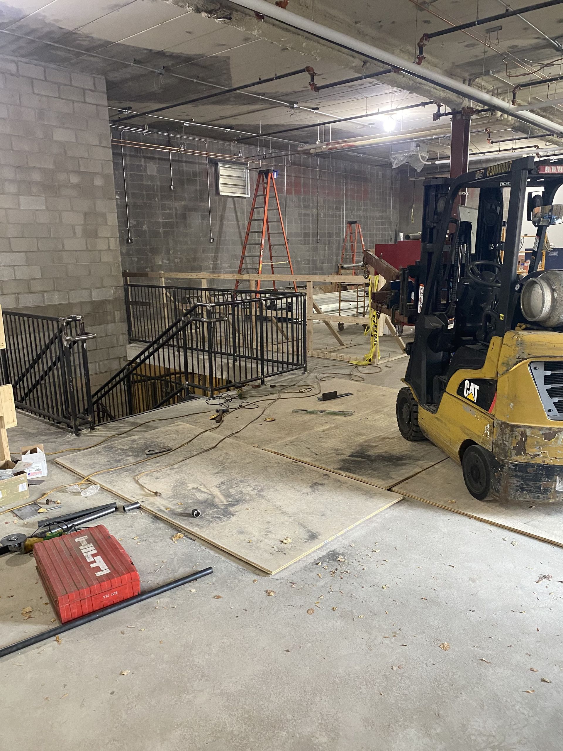 Construction site: stairs, forklift, tools, cinder block walls, exposed pipes.