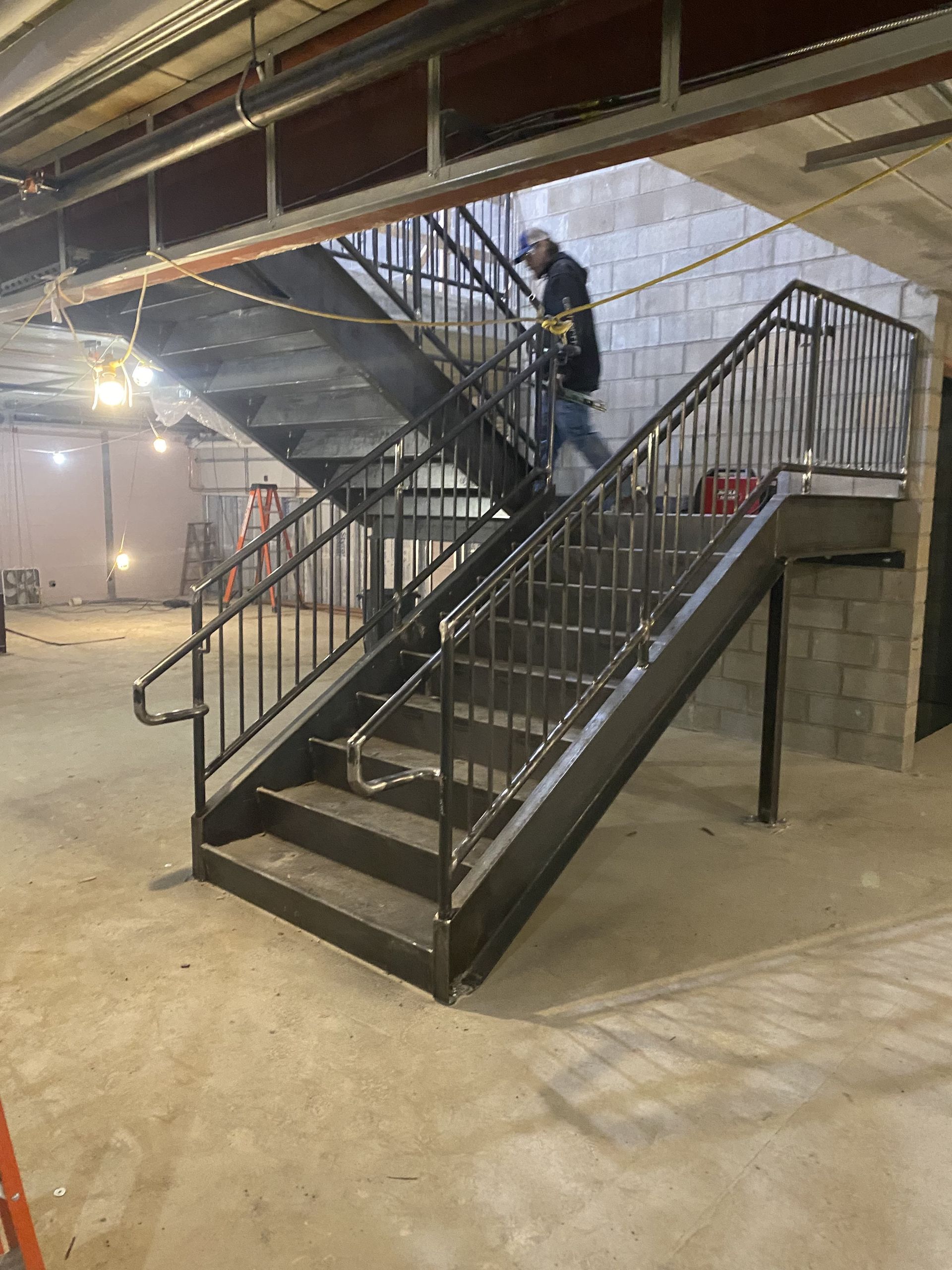 Construction site: A person walks down metal stairs with handrails. Concrete block wall in the background.
