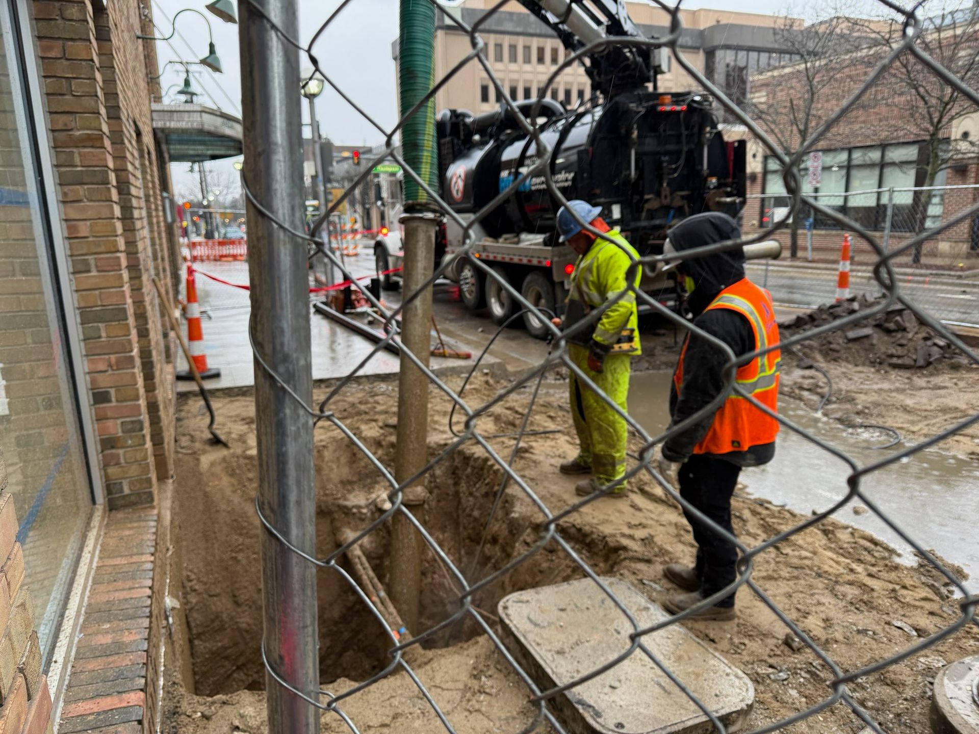 Construction workers near a ditch with a truck, behind a chain-link fence.