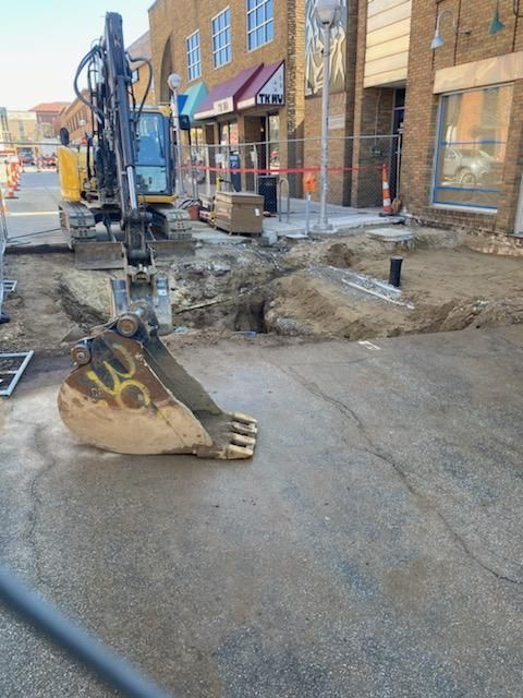Excavator in street digging up pavement; construction site with barriers.