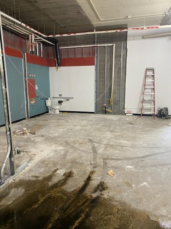 Interior demolition: Exposed pipes, partially demolished walls, toilet, ladder, and debris on concrete floor.
