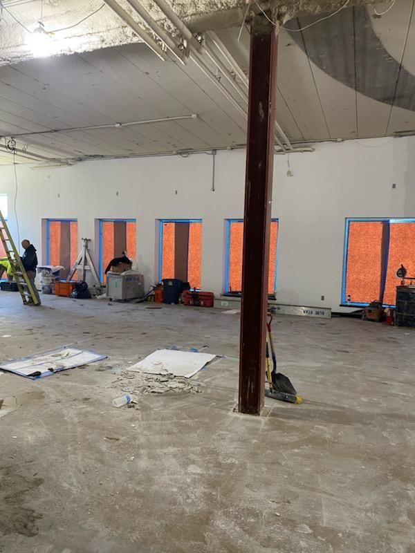 Interior of a building under construction, exposed beams, unfinished floors, windows covered in orange material.