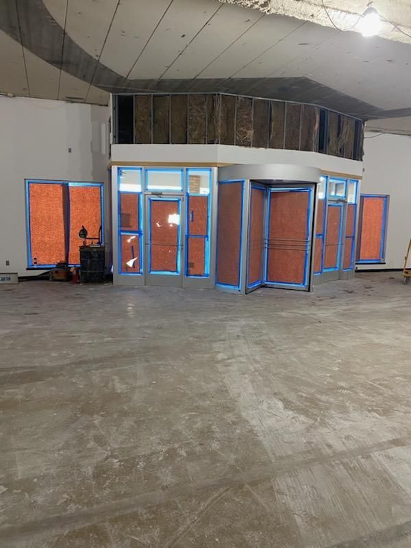 Construction site: Storefront with orange barrier tape on windows. Gray concrete floor, exposed insulation overhead.