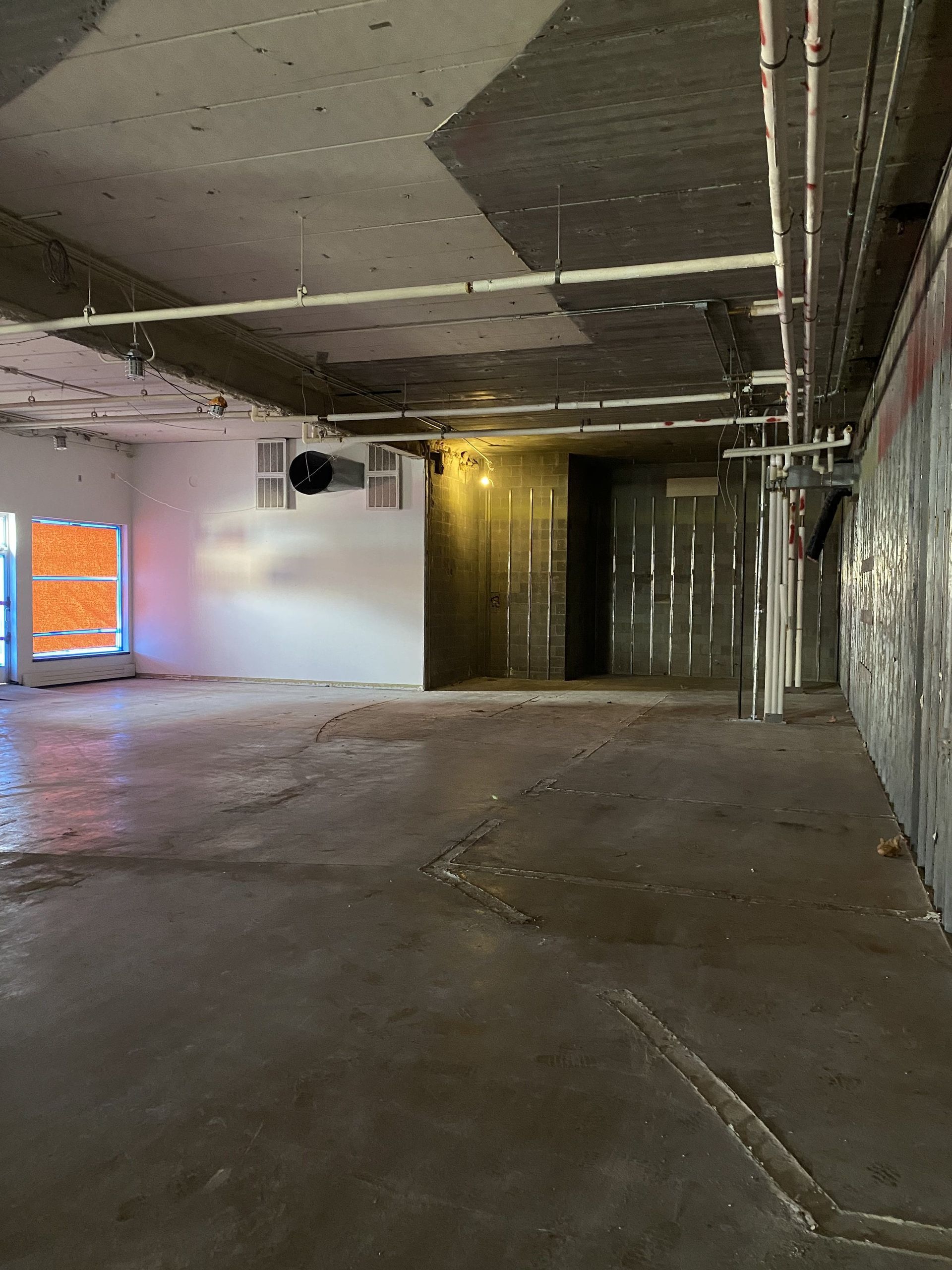 Empty interior room with concrete floor, exposed pipes, unfinished walls, and doorway.