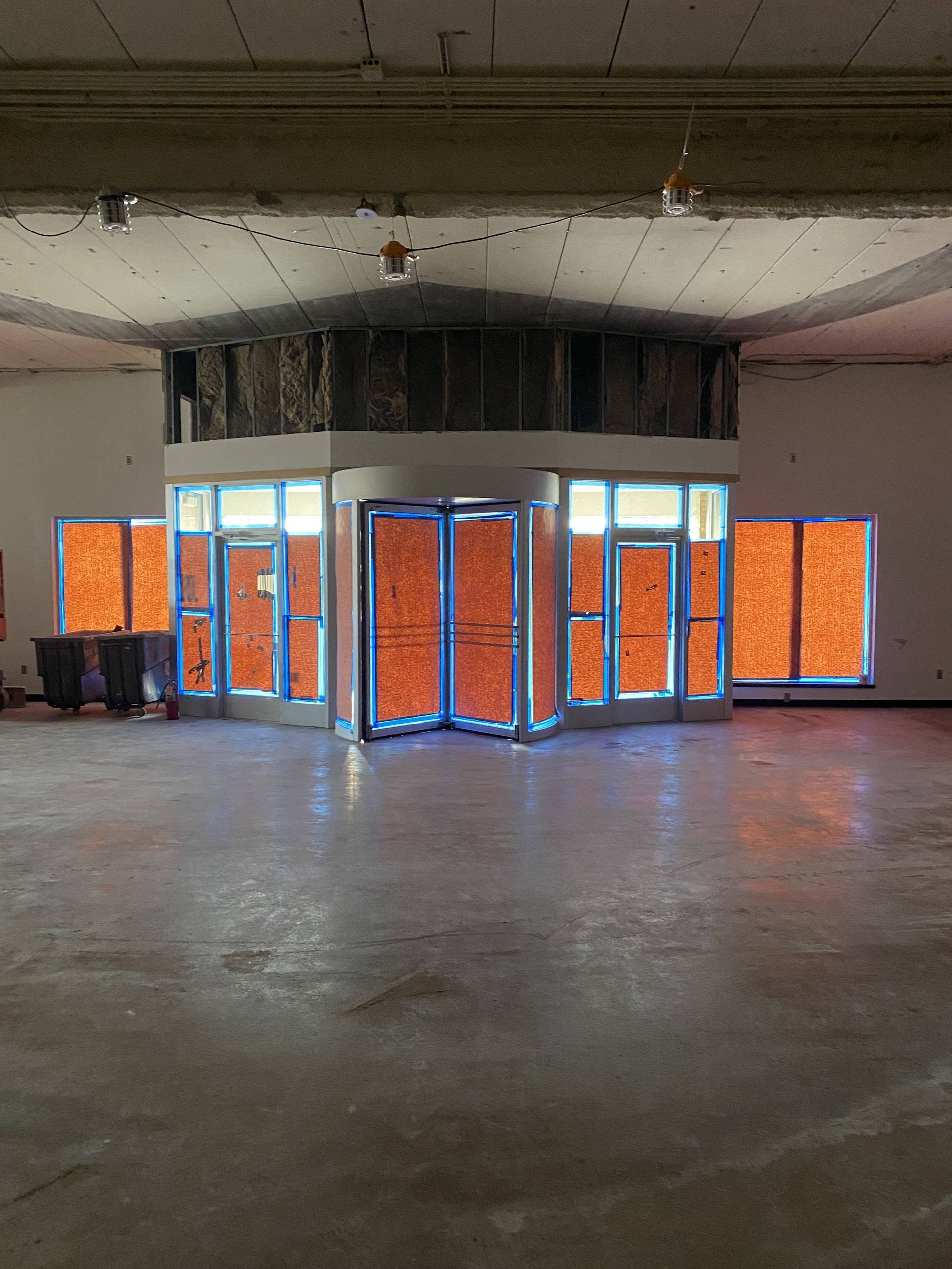 Orange-covered windows and doors with blue tape. Inside a round building, dusty interior, dim lighting.