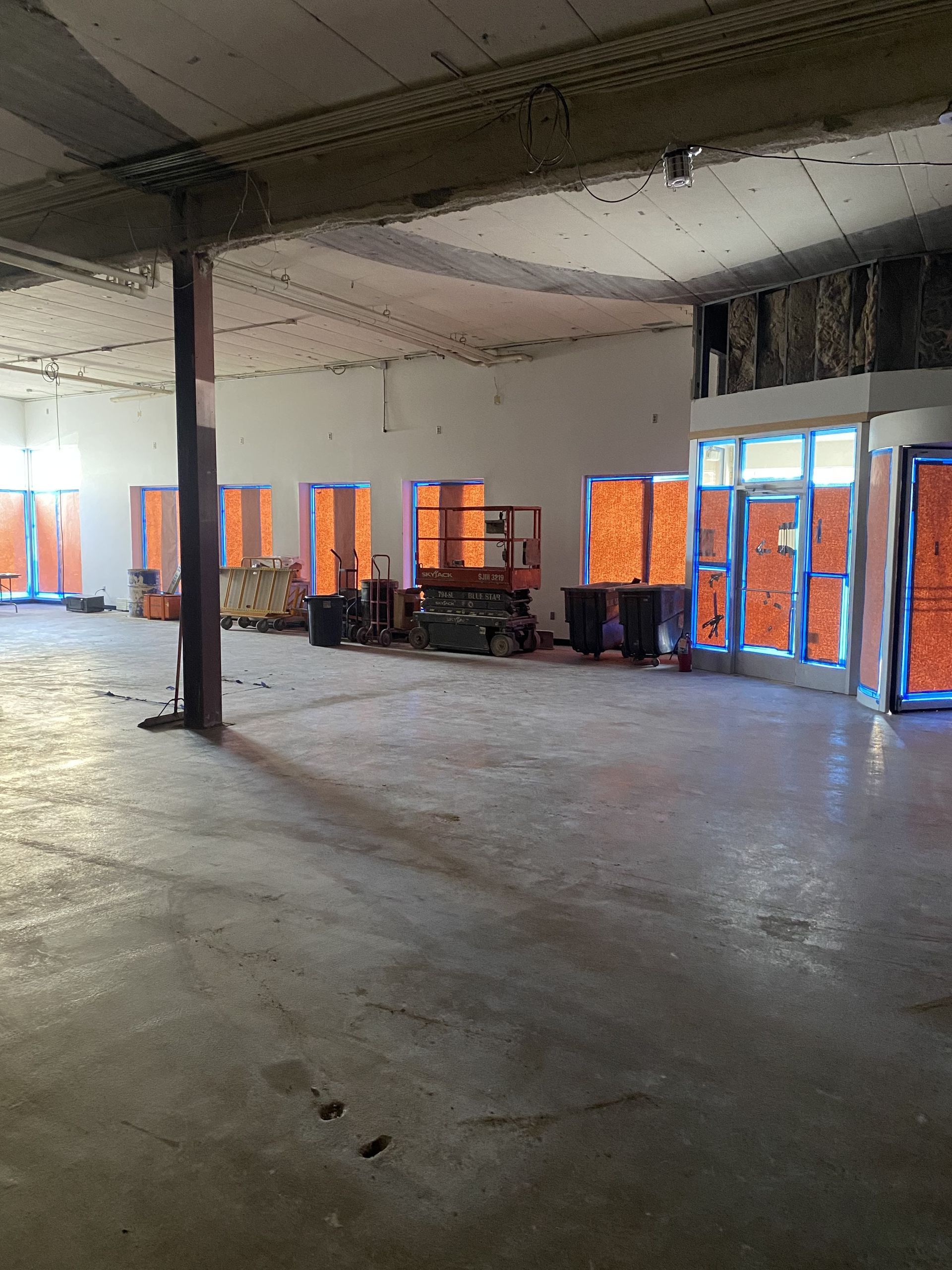 Interior construction site with concrete floor, unfinished walls, and orange taped windows.