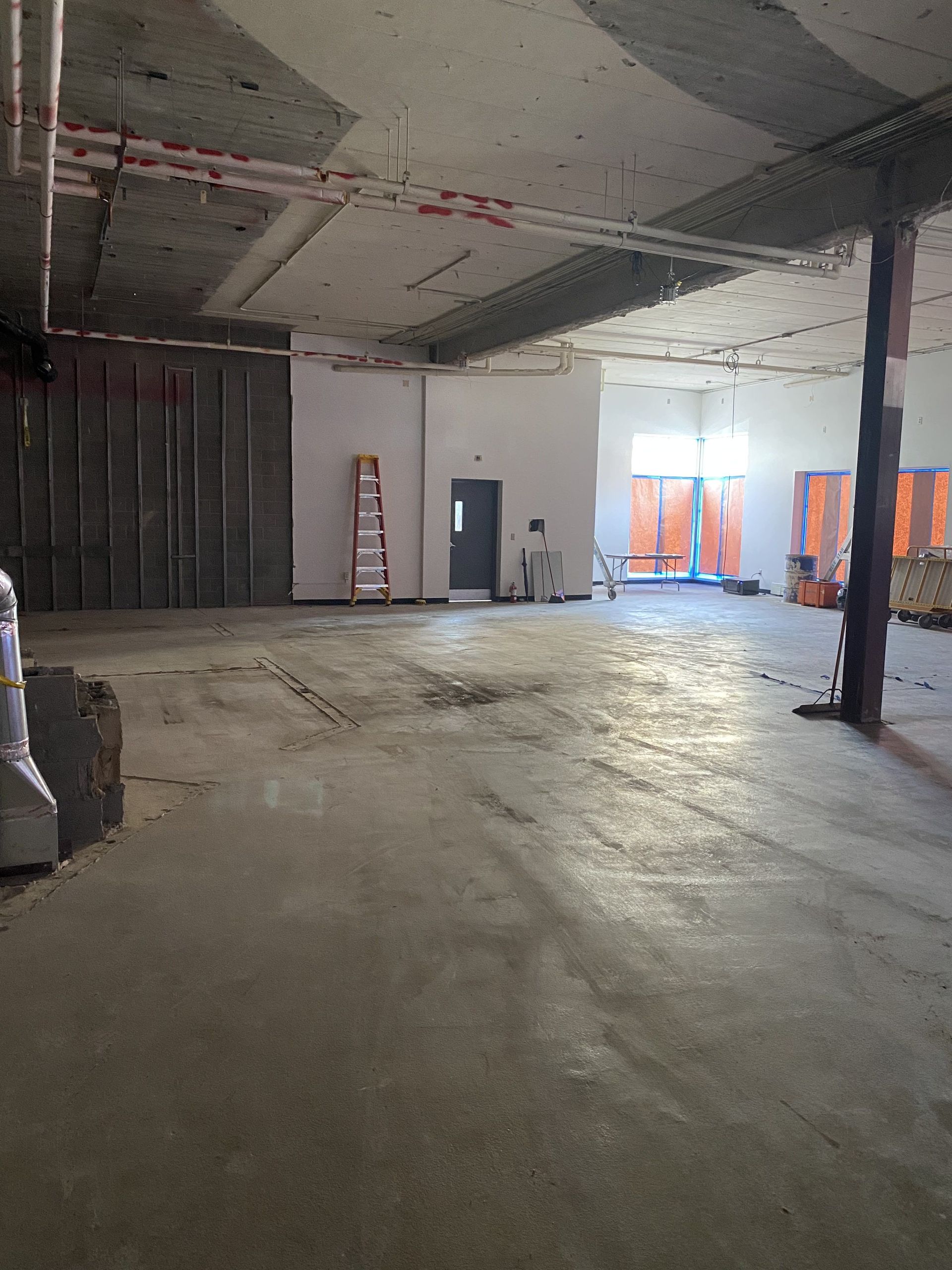 Construction site interior with exposed concrete and metal, ladder, and doorway.