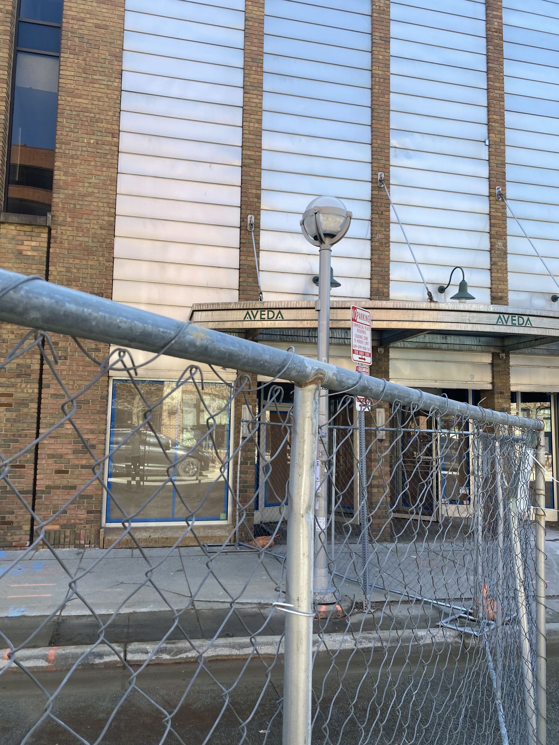 A building with vertical frosted glass panels behind a chain-link fence.