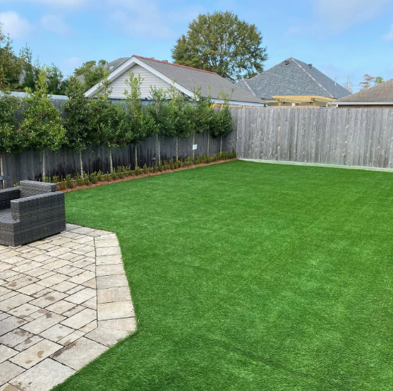 Green backyard with artificial turf, stone patio, wooden fence, and hedges.