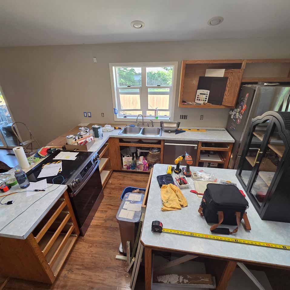 Kitchen under renovation with cabinets, tools, and materials spread across the counters and floor.