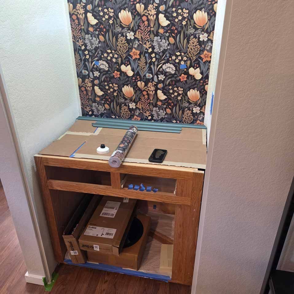 Small wooden cabinet in a hallway with tools and boxes on top and inside, against patterned wallpaper.