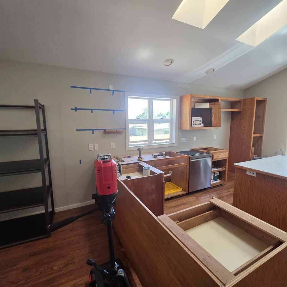 Unfinished kitchen with cabinets, countertops, shelves, and a red vacuum on a wood floor.