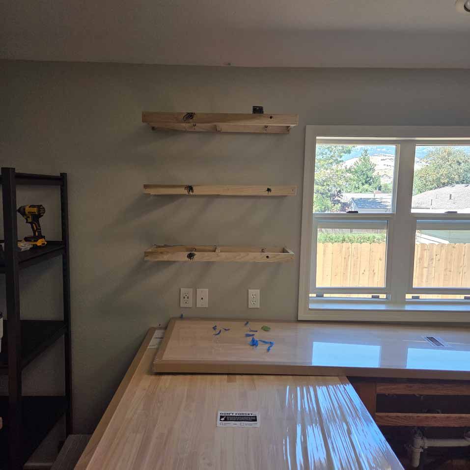 Wooden shelves mounted on a gray wall beside a window in a bright room with a workbench.