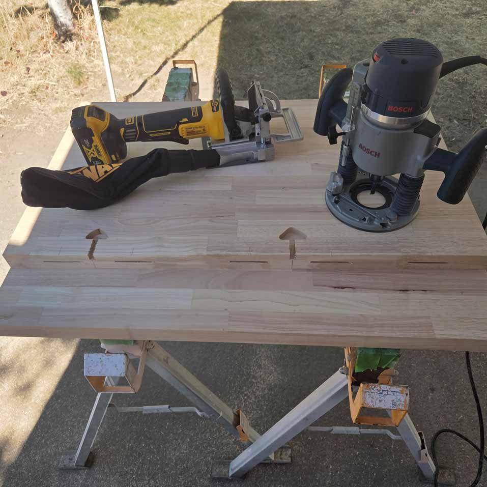 Wooden board on sawhorses with a router, circular saw, and tape measure outdoors
