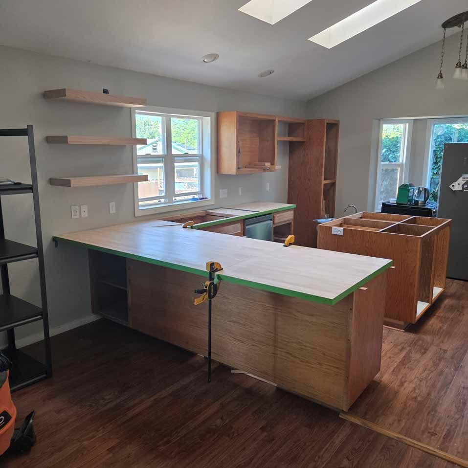 Empty kitchen with unfinished cabinets, wood floors, white walls, and a large island under construction