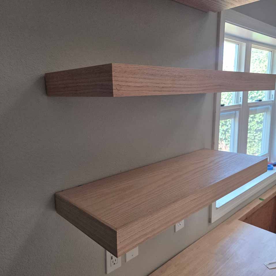 Two floating wooden shelves mounted on a gray wall beside a window.