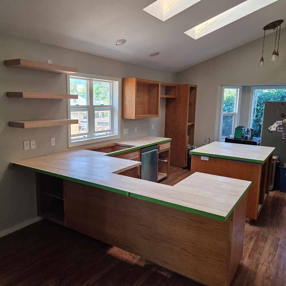 Empty kitchen with unfinished wood cabinets, dark floors, skylights, and a green-topped island.