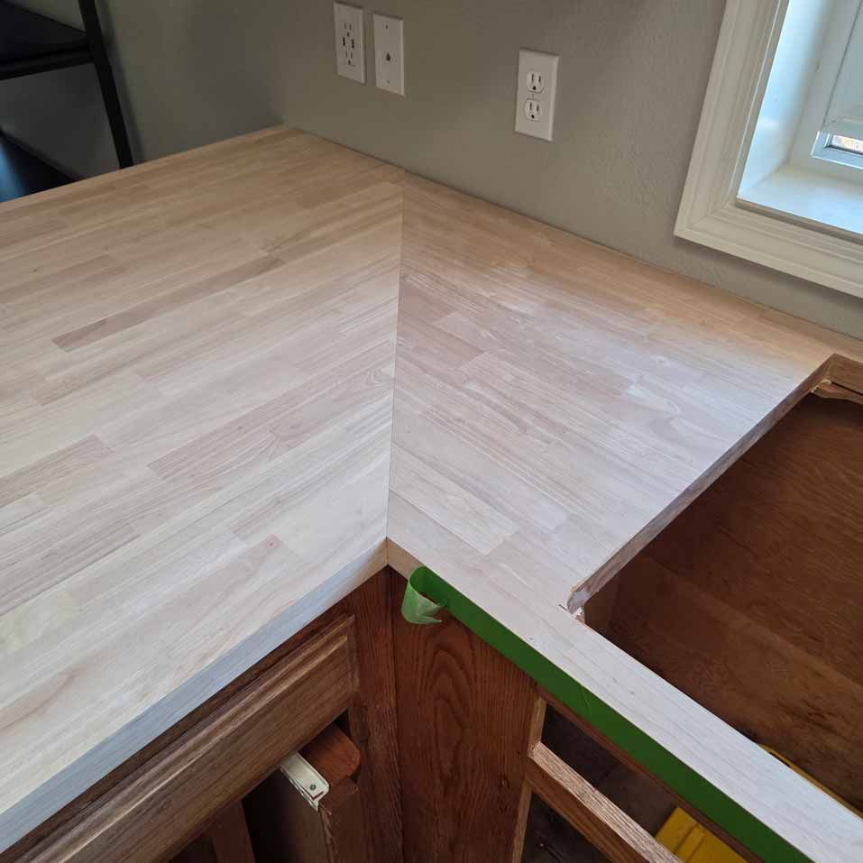 Corner of a light wood countertop in a room with wall outlets and a window