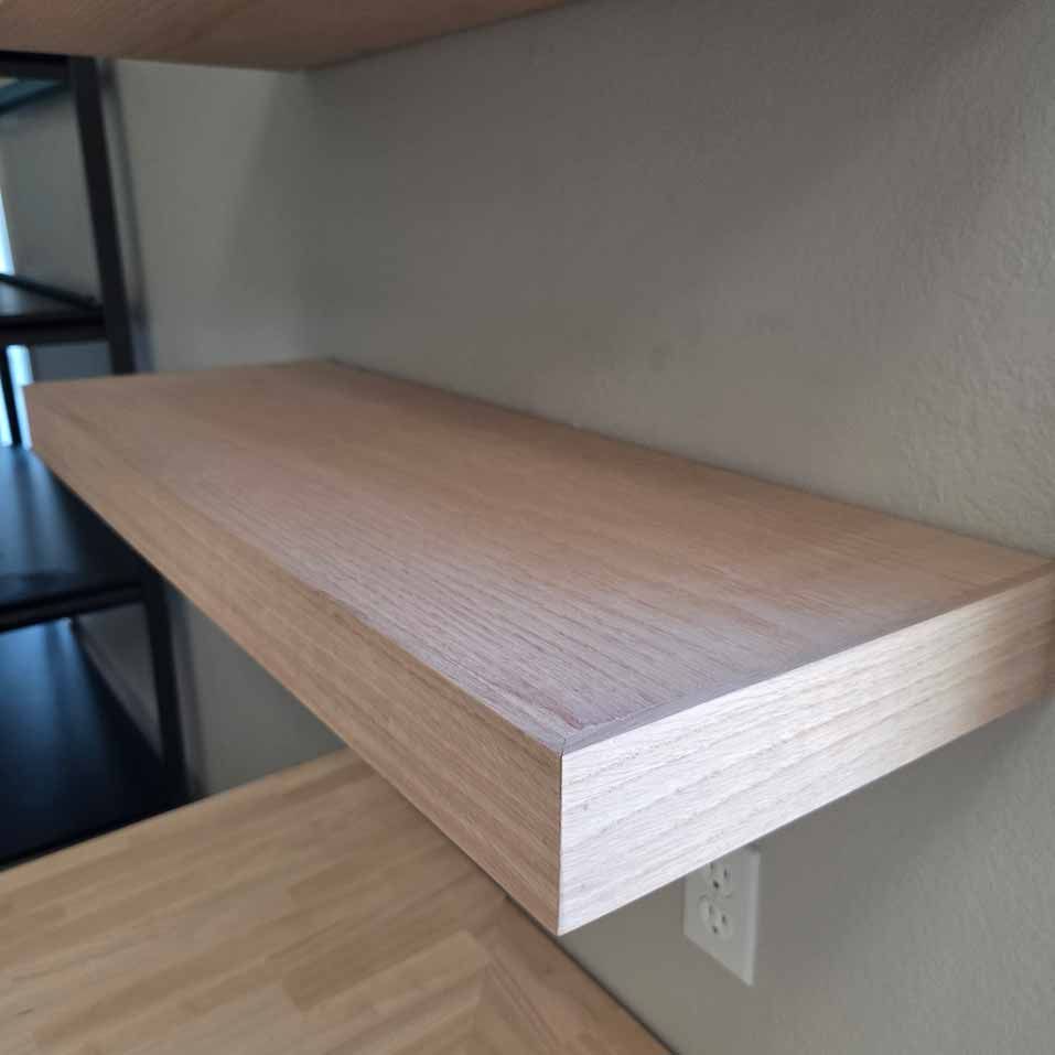 Floating light wood shelf mounted on a beige wall above an electrical outlet