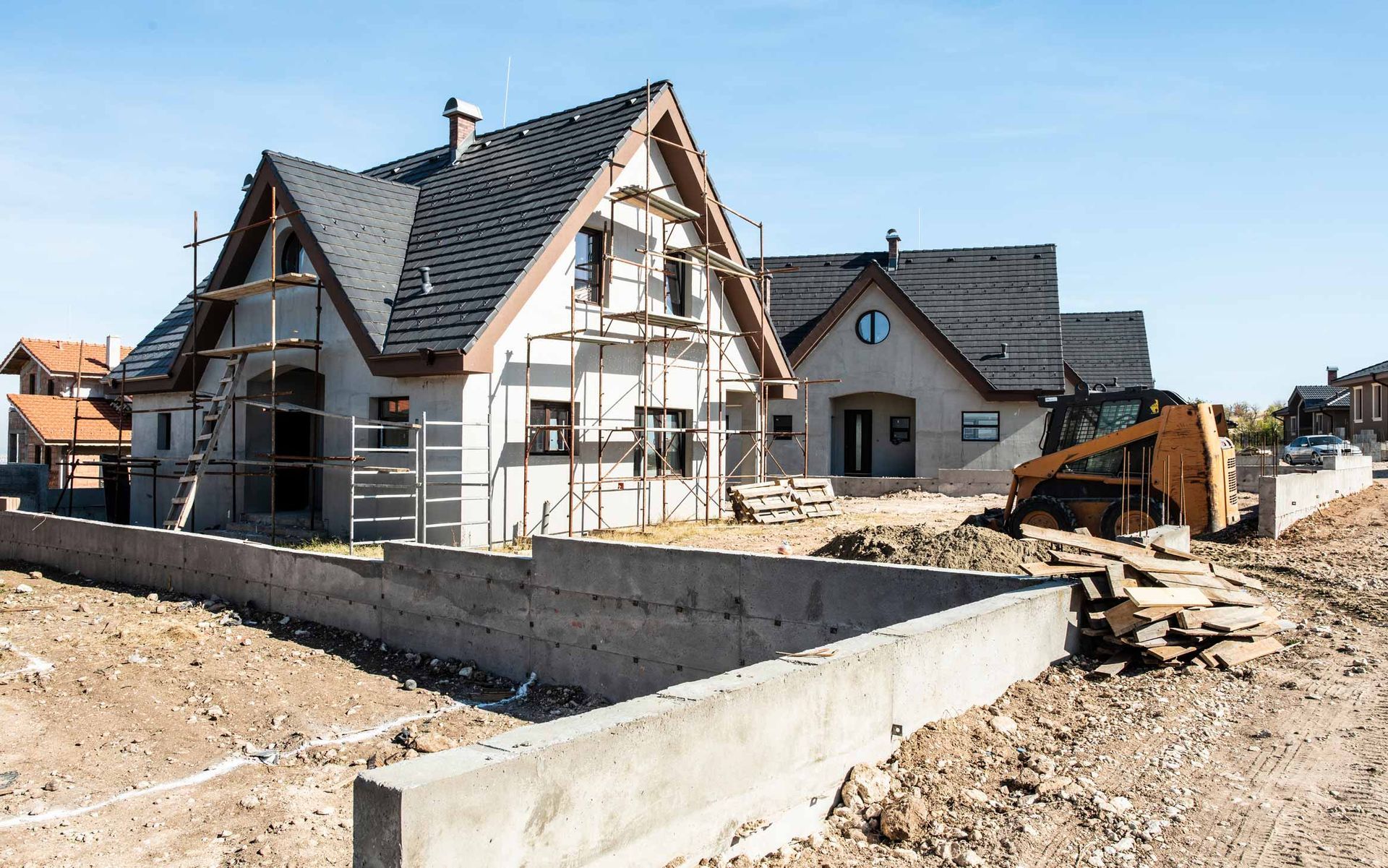 New house under construction with unfinished roof, concrete foundation, and dirt lot