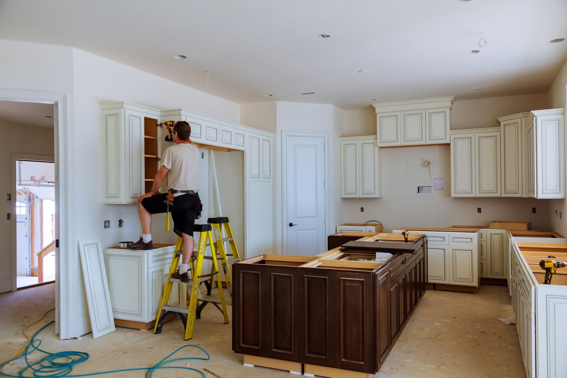A man is standing on a ladder in a kitchen under construction.