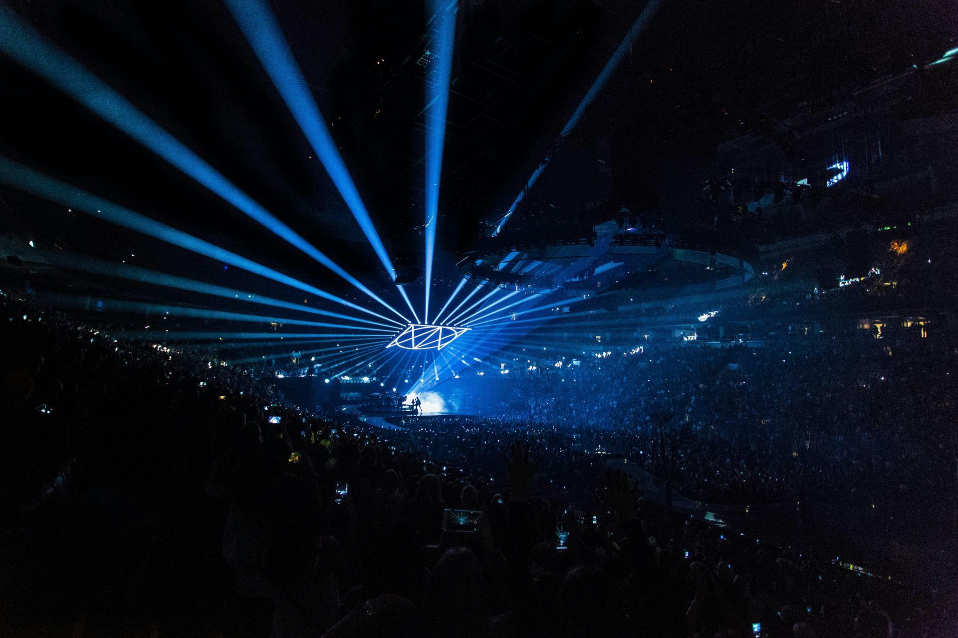 A crowd of people watching a concert with blue lights coming out of the ceiling