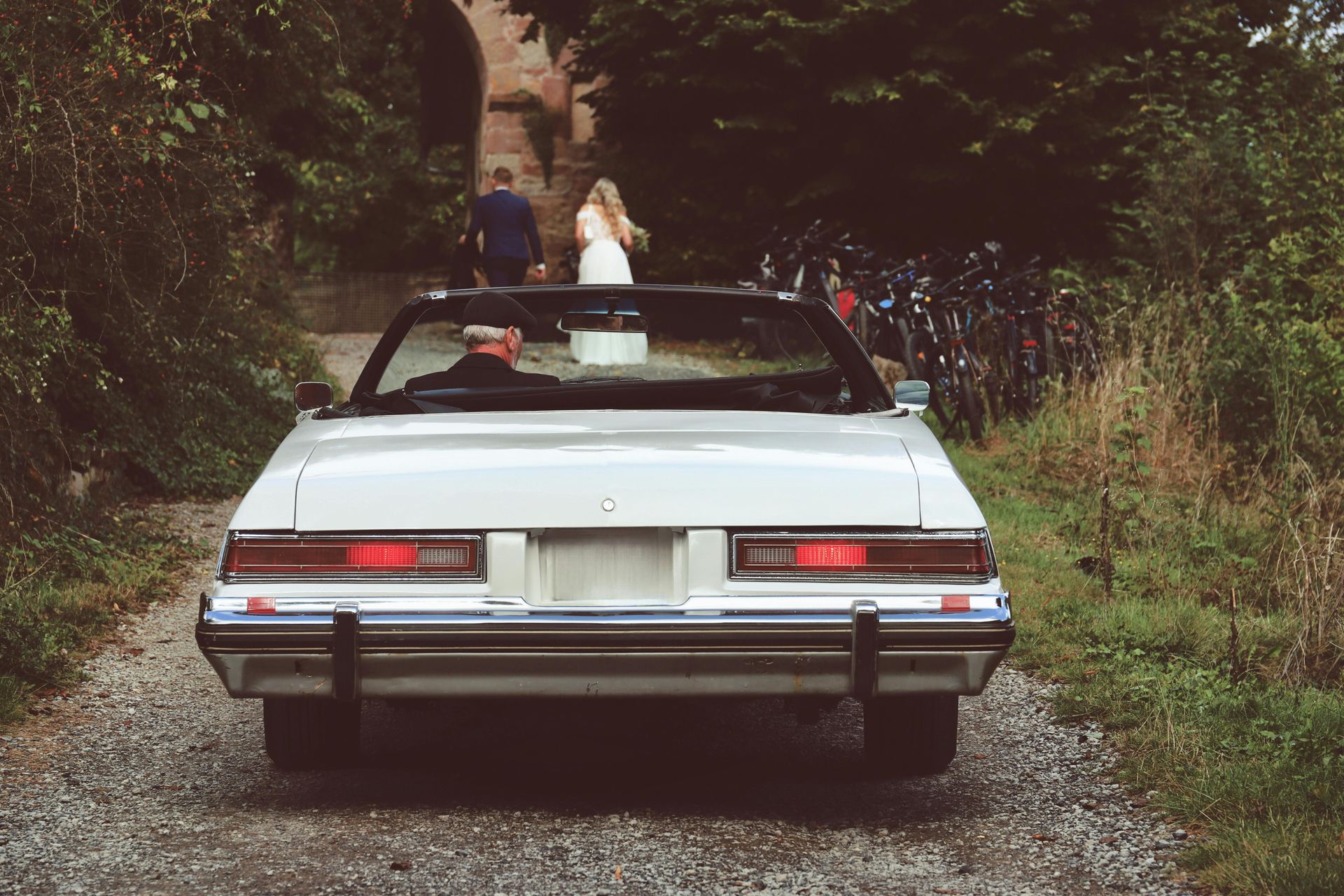 A white convertible car is parked on a gravel road.