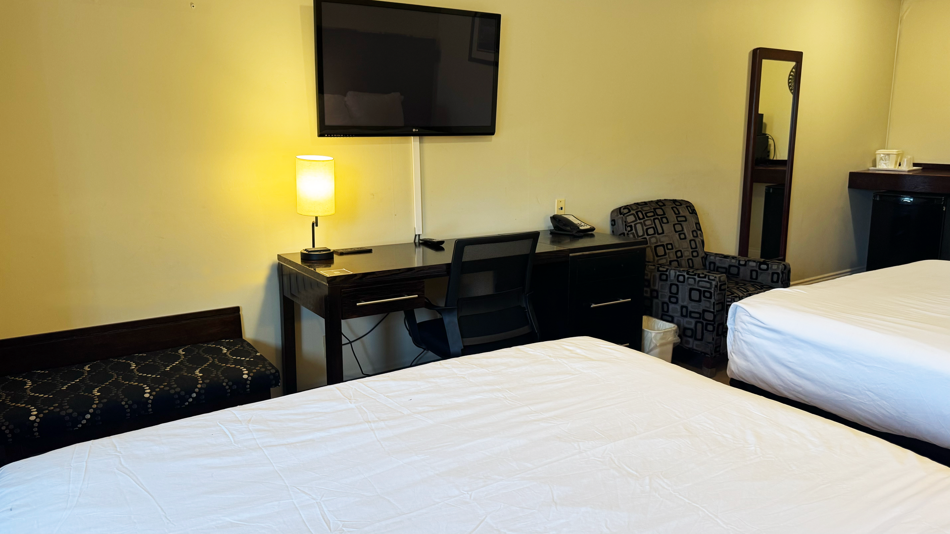 Hotel room with two beds, desk with TV, chair, lamp, and mirror.