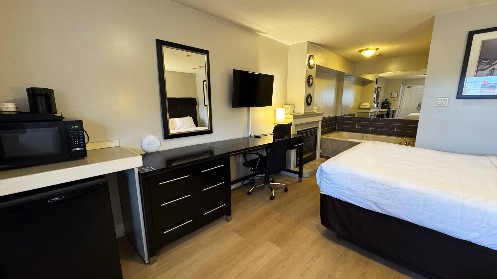 Hotel room with bed, desk, mirror, TV, microwave, and fireplace.