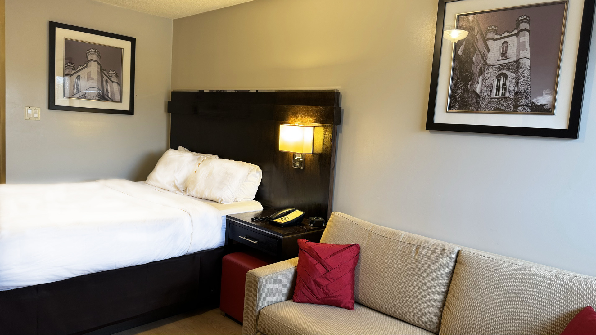 Bedroom with a bed, small sofa, artwork, and a nightstand with a lamp and phone.