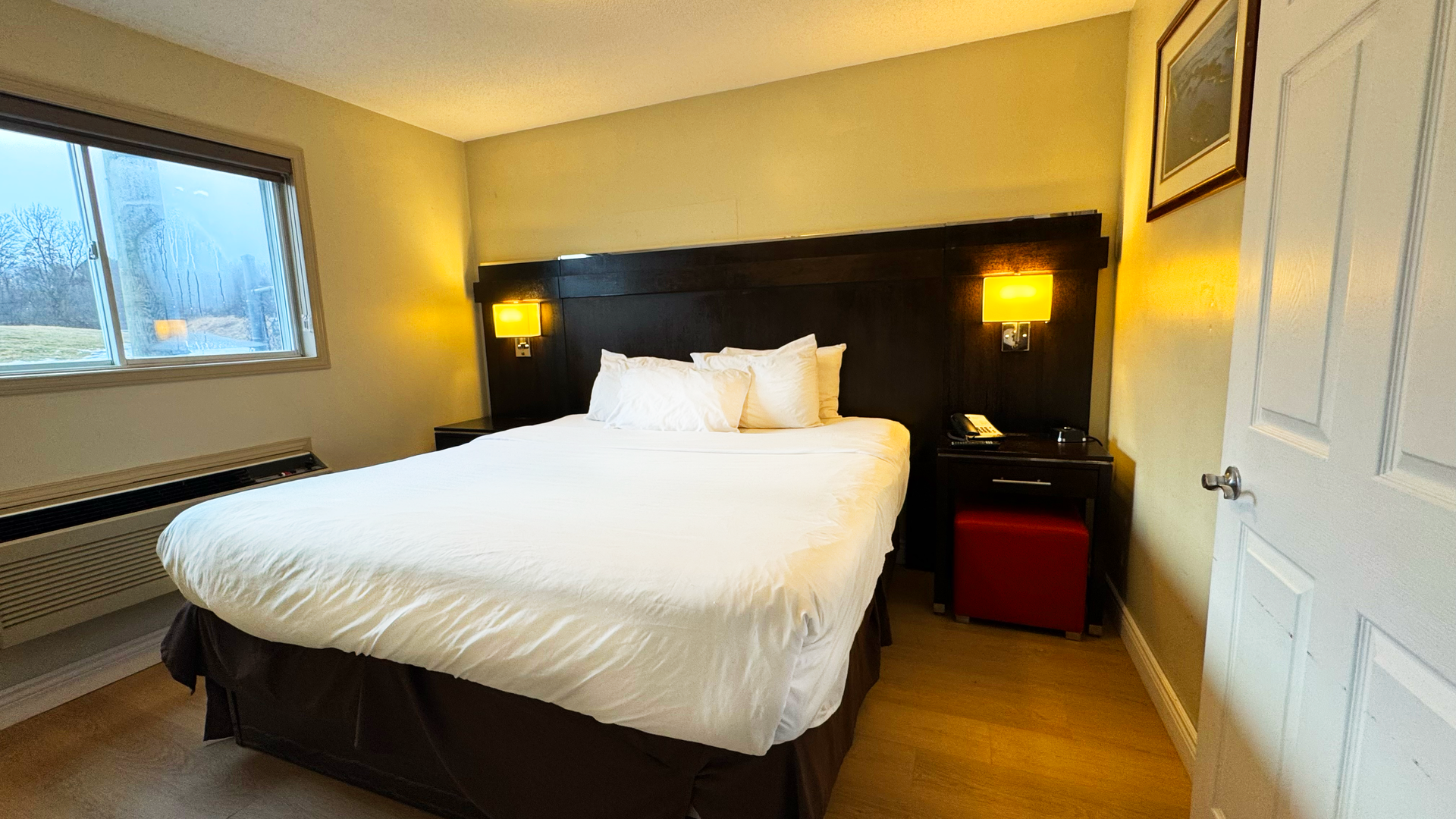 Hotel room with bed, bedside table, window, and door in a separate bedroom