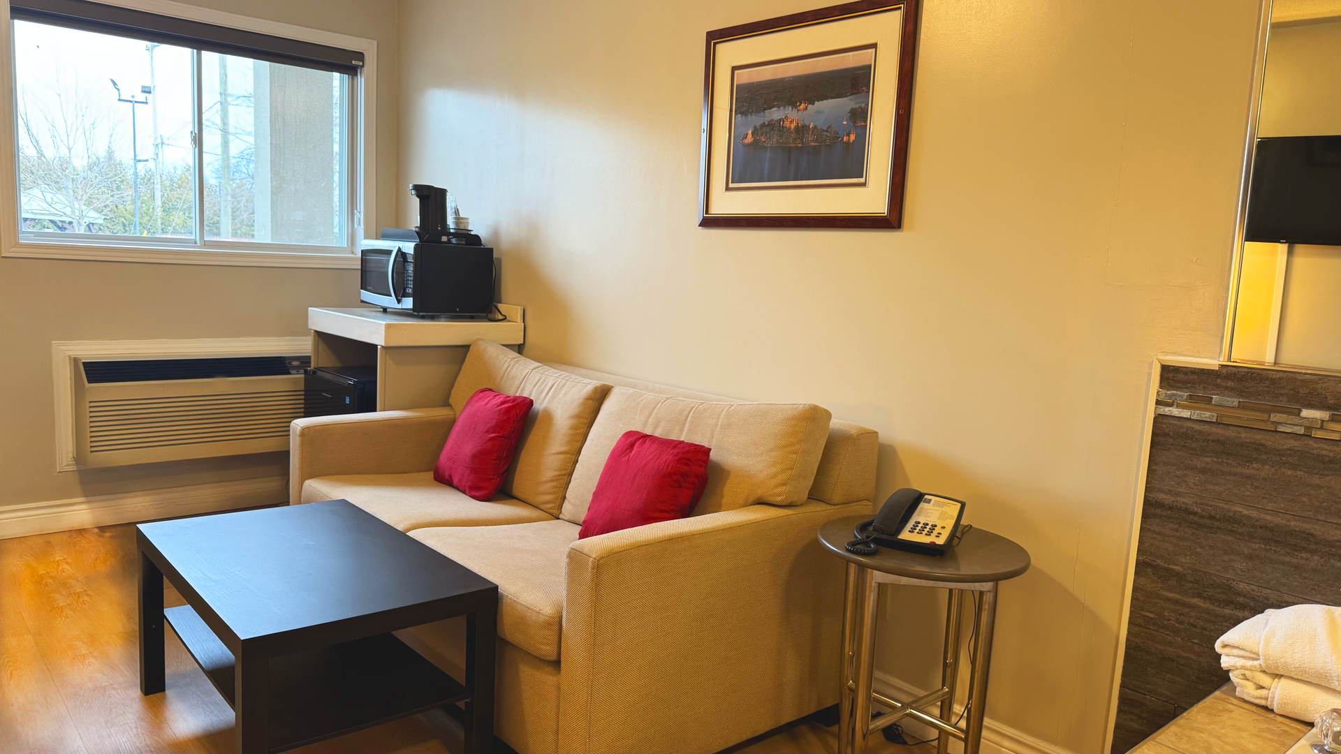 Small hotel room with a couch, table, microwave, and window.