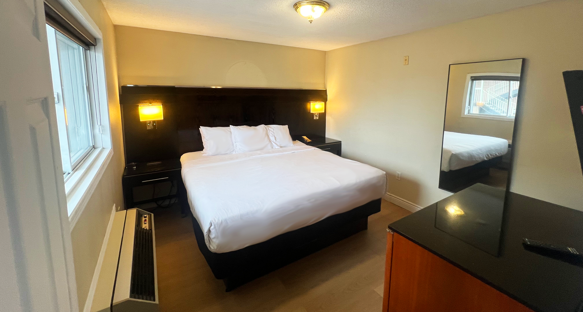 Hotel room with a king-sized bed, nightstands, and a dresser. There is a window and a mirror.
