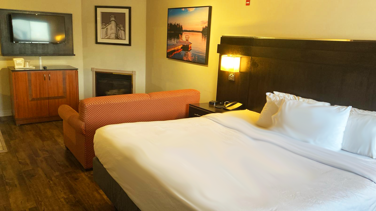 Hotel room with a bed, small sofa, fireplace, TV, and artwork.