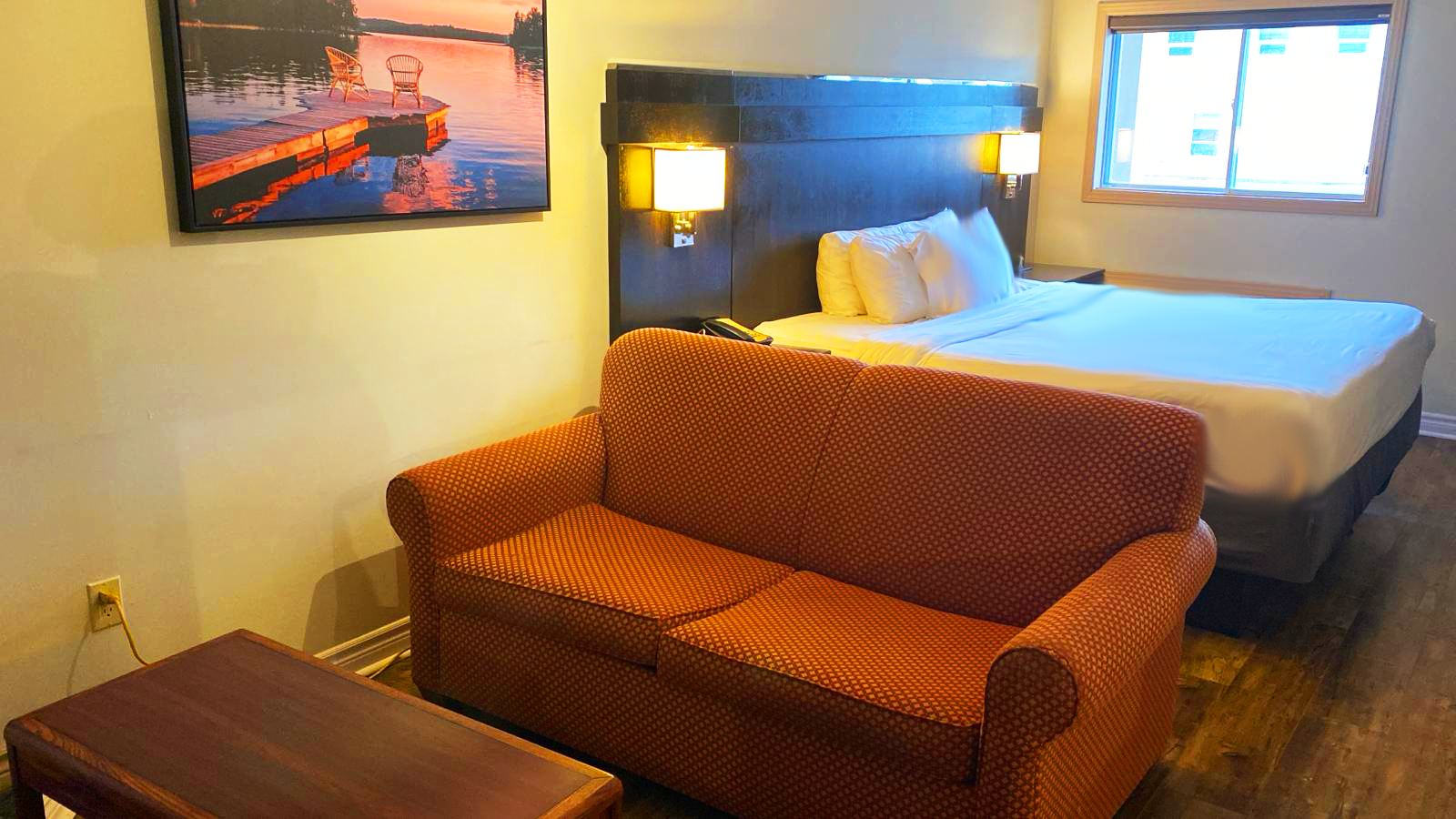 Hotel room with a  sofa, bed, window, and landscape art.