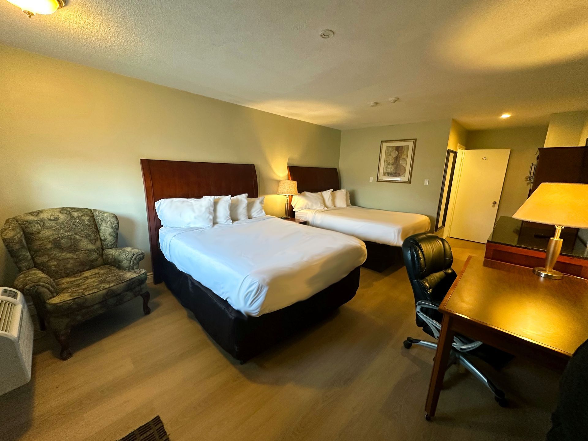a hotel room with two beds , a chair , a desk and a lamp .