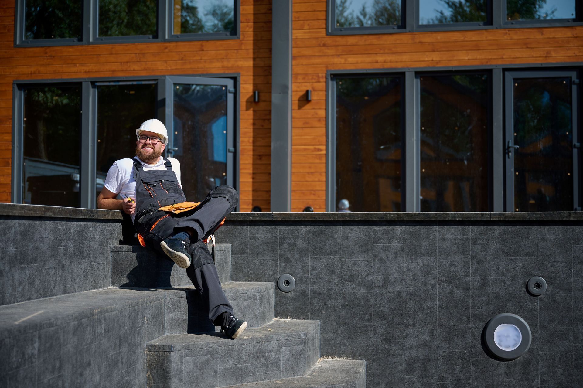 A smiling contractor sitting on the steps of an empty swimming pool.