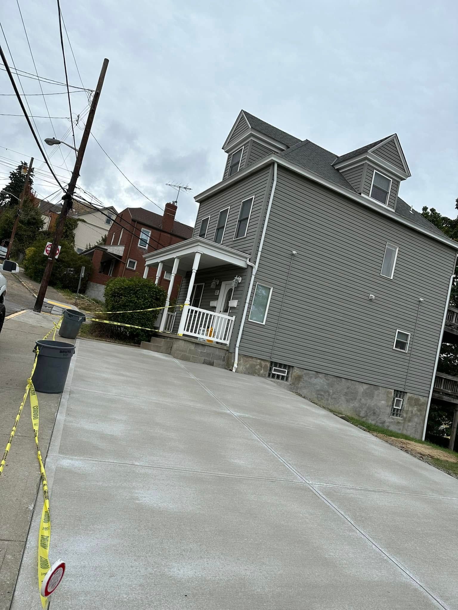 Steep concrete driveway beside a gray house with white trim on a cloudy day