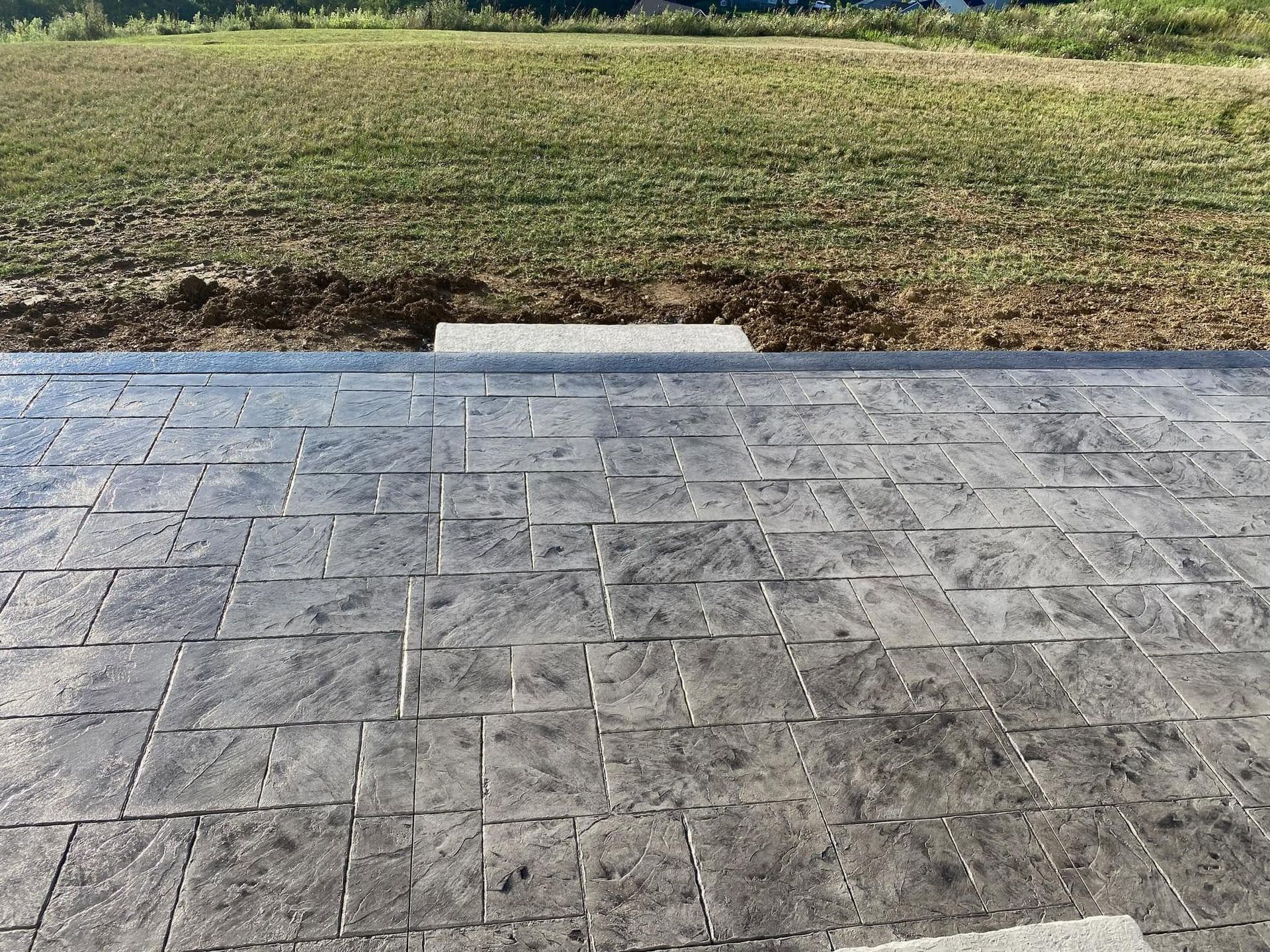 Empty stone patio with a grassy yard and a small concrete step in the center.
